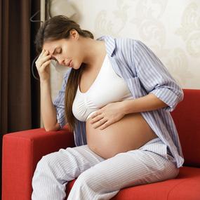 Schwangere Frau sitzt auf dem Sofa und hält sich den Kopf