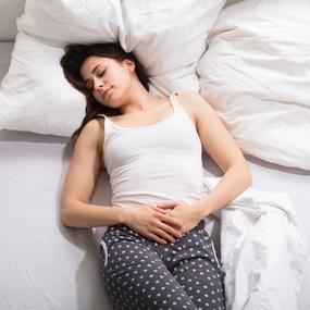 Frau liegt mit Unterleibschmerzen im Bett