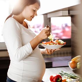 Schwangere Frau isst und bereitet Essen vor