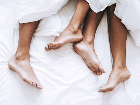 Paar im Bett mit Füßen aus der Decke