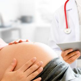 Schwangere Frau fühlt Babybauch beim Arzt