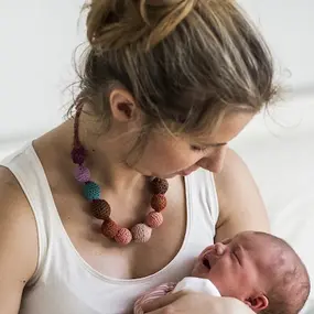 Mutter sitzt auf einem Bett und hält Baby im Arm