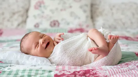 Baby liegt strahlend und lachend im Bett