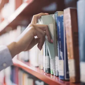 Person holt Buch aus dem Bücherregal