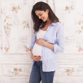 Schwangere Frau lächelt und hält schwangeren Bauch