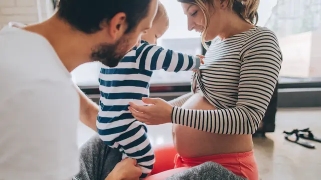 Mann hält kleines Kind das den Bauch der schwangeren Mutter berührt