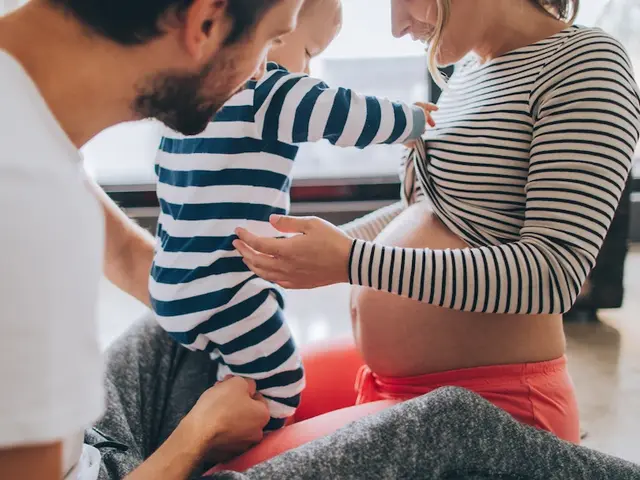 Mann hält kleines Kind das den Bauch der schwangeren Mutter berührt