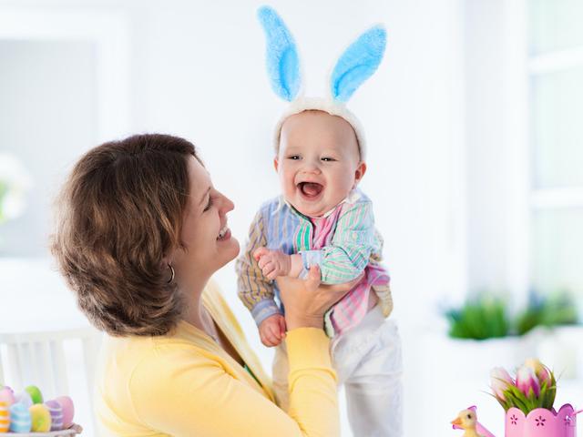 Ostern mit Baby feiern - Mutter hält Baby mit Babyohren auf dem Arm. Beide freuen sich.