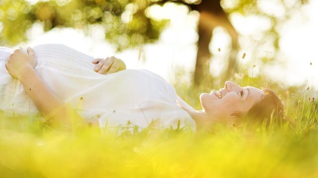 Schwangere Frau liegt lächelnd im Gras