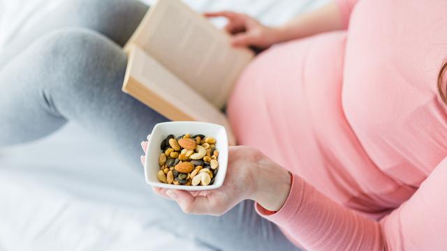 Schwangere Frau liest Buch und isst parallel
