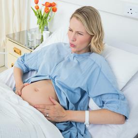 Schwangere Frau liegt im Krankenhaus und hält sich Bauch