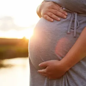 Schwangere Frau hält Bauch bei Sonnenuntergang