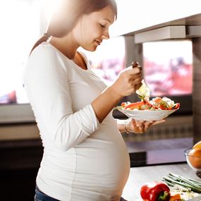 Schwangere bereitet Salat mit Öl vor