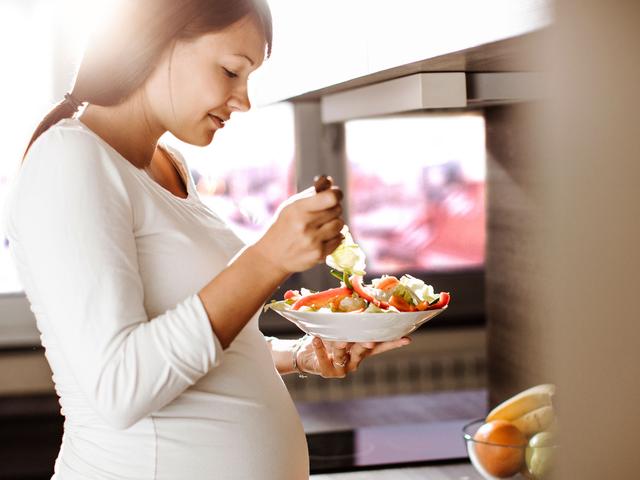 Schwangere Frau isst und bereitet Essen vor