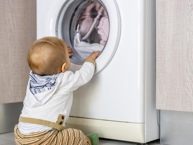 Baby sitzt vor Waschmaschine