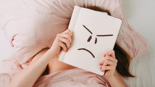 Frau liegt enttäuscht mit Mappe vor dem Gesicht im Bett