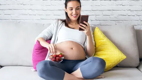 Schwangere sitzt auf dem Sofa am Handy