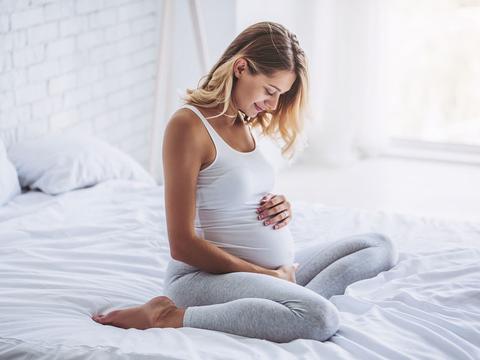 Schwangere Frau hält Ihren Bauch und sitzt auf dem Bett