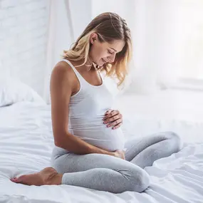 Schwangere Frau hält Ihren Bauch und sitzt auf dem Bett