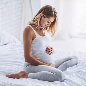 Schwangere Frau hält Ihren Bauch und sitzt auf dem Bett