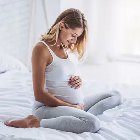 Schwangere Frau hält Ihren Bauch und sitzt auf dem Bett