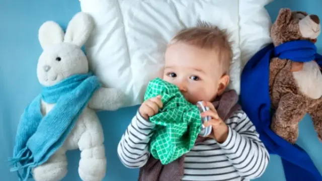 Baby liegt erkältet mit Kuscheltieren im Bett