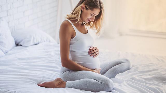 Schwangere Frau auf Bett hält Bauch