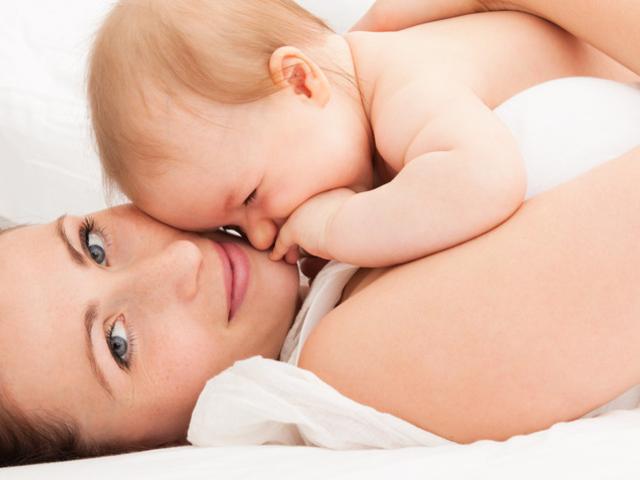 Frau liegt mit Baby auf der Brust im Bett