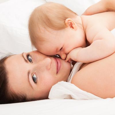 Frau liegt mit Baby auf der Brust im Bett