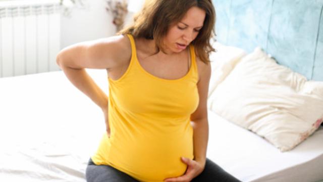 Schwangere Frau mit Beschwerden sitzt auf der Bettkante