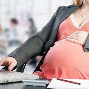 Schwangere Frau sitzt zur Arbeit am Laptop