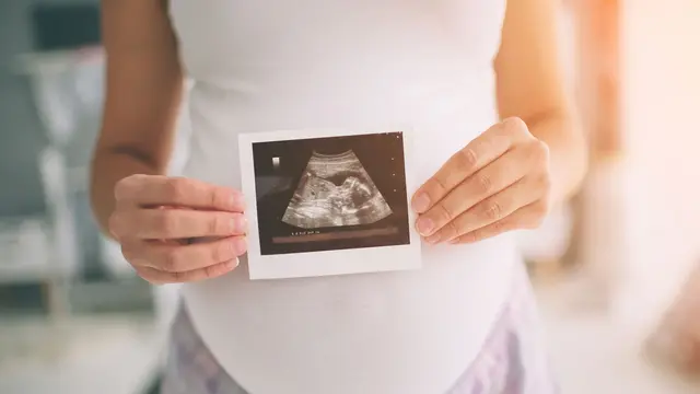 Schwangere Frau hält Ultraschallbild in die Kamera