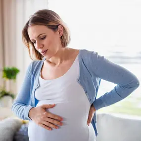 Schwangere Frau hält sich den Bauch und Rücken