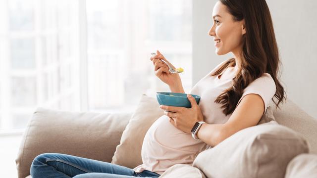 Schwangere Frau sitzt auf dem Sofa und isst