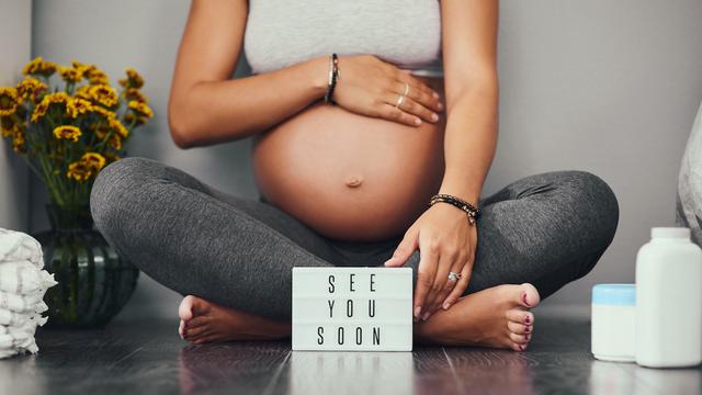 Schwangere Frau hält Ihren Bauch und sitzt auf dem Boden