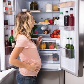Schwangere Frau steht vor Kühlschrank