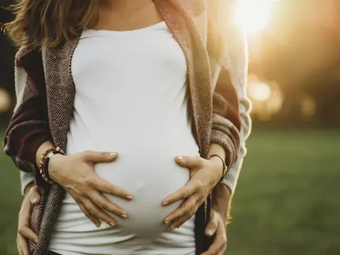 Eine schwangere Frau mit einem Babybauch wird von hinten umarmt