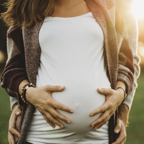Eine schwangere Frau mit einem Babybauch wird von hinten umarmt
