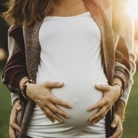 Eine schwangere Frau mit einem Babybauch wird von hinten umarmt