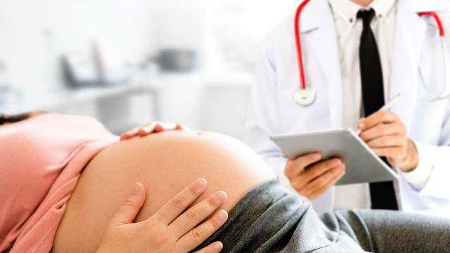 Schwangere Frau fühlt Babybauch beim Arzt
