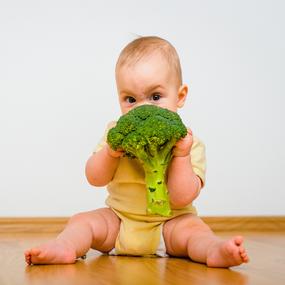 Baby mit Brokkoli in der Hand