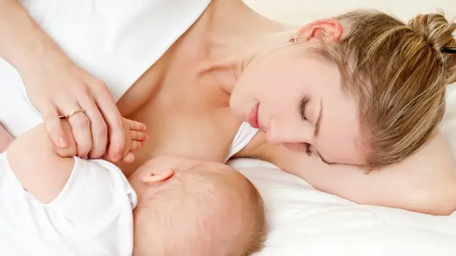 Mutter liegend stillt Baby mit Kopf zur Kamera