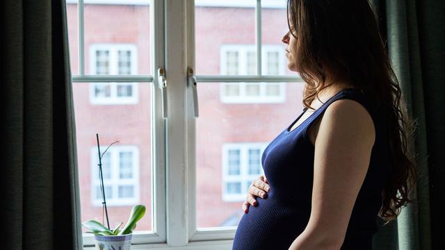 Schwangere Frau steht am Fenster und hält Bauch