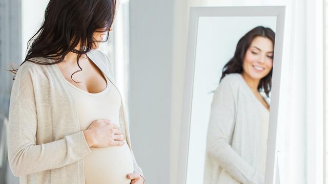Schwangere Frau schaut sich im Spiegel an