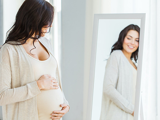 Schwangere schaut sich im Spiegel an