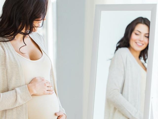 Schwangere schaut sich im Spiegel an