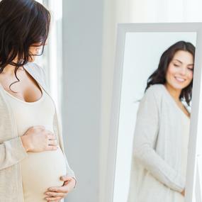 Schwangere Frau schaut sich im Spiegel an