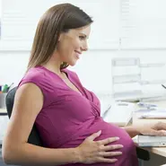 Schwangere Frau sitzt lächelnd am Laptop