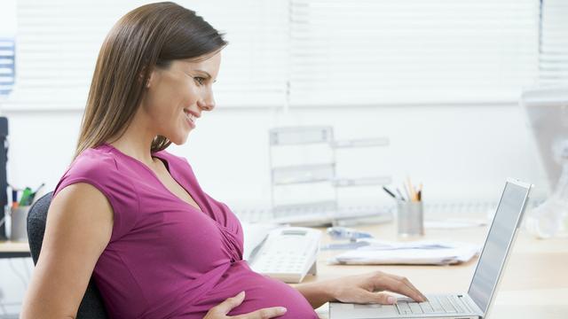 Schwangere Frau sitzt lächelnd am Laptop