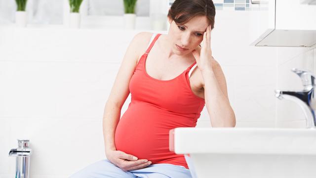 Schwangere Frau im Badezimmer fässt sich an Kopf